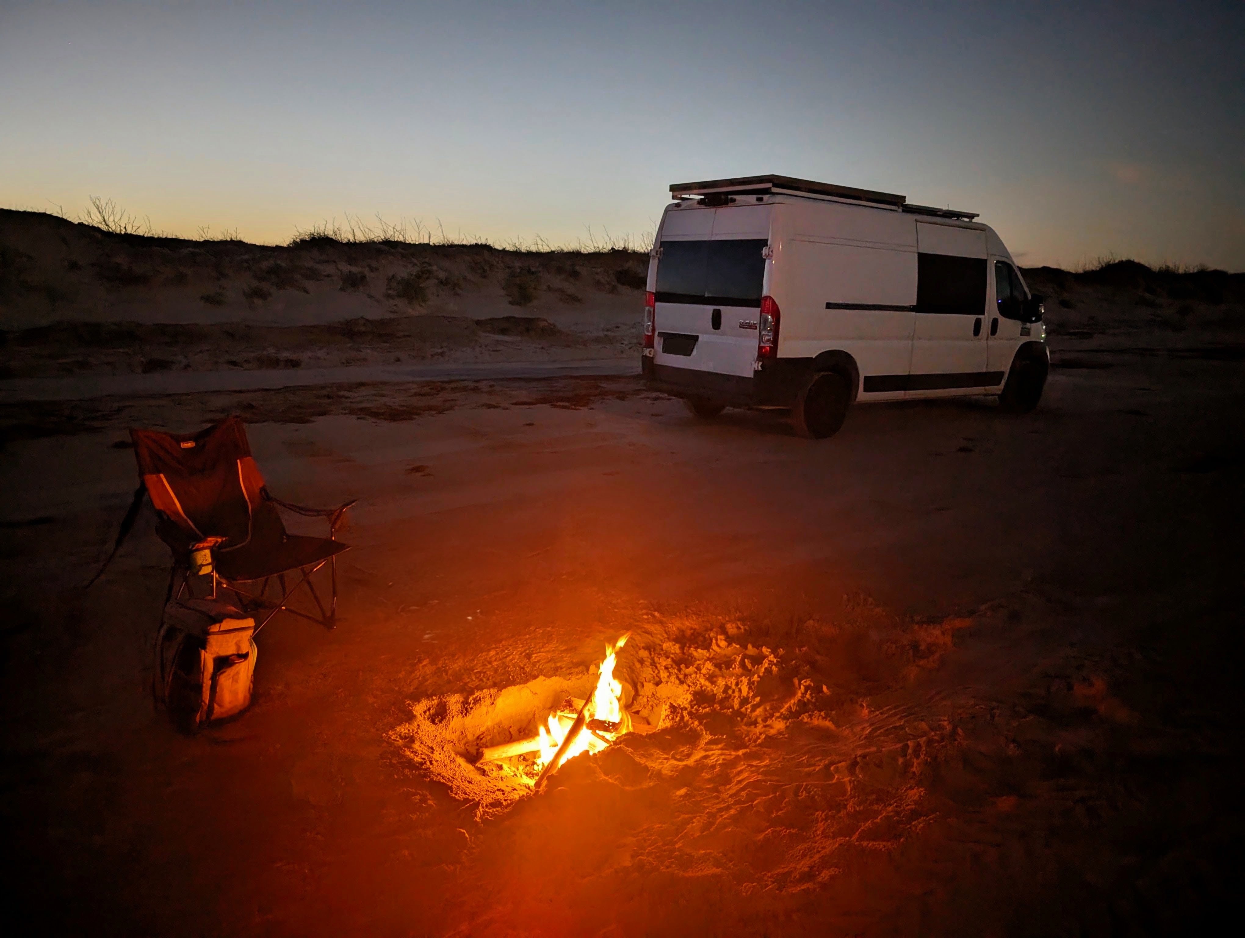 A camper van and beach campfire at dusk on the Gulf shore