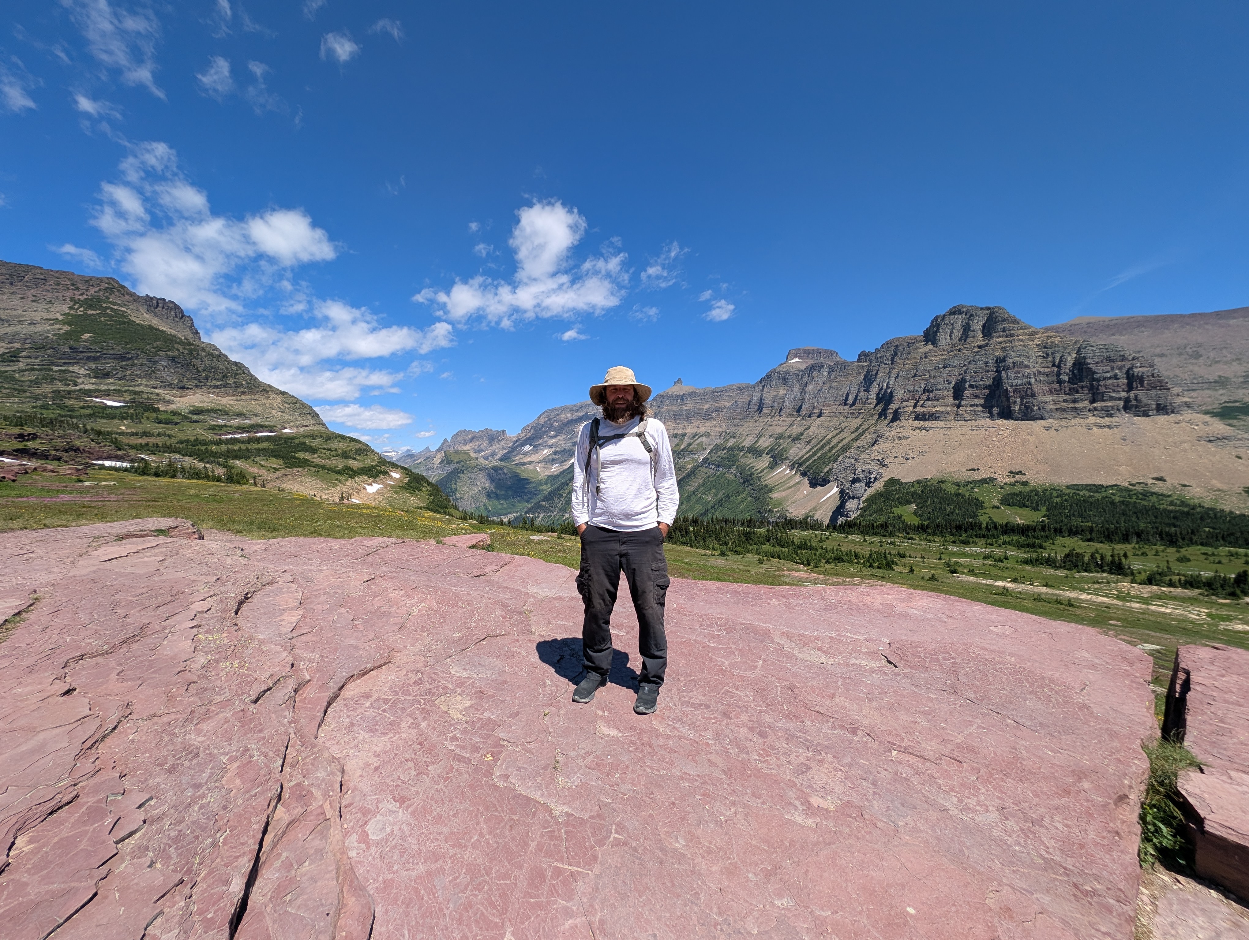 A hiker in a sun hat on a high pass in Glacier National Park