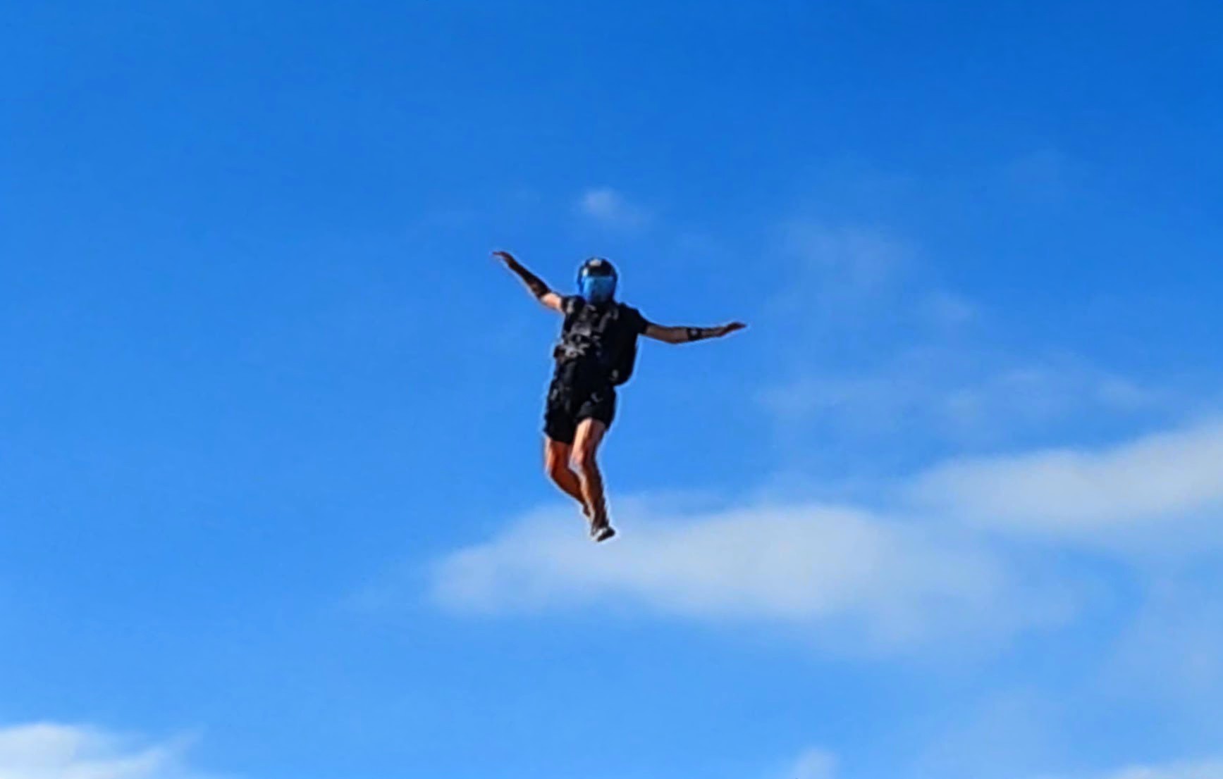 A skydiver in freefall against a clear blue sky
