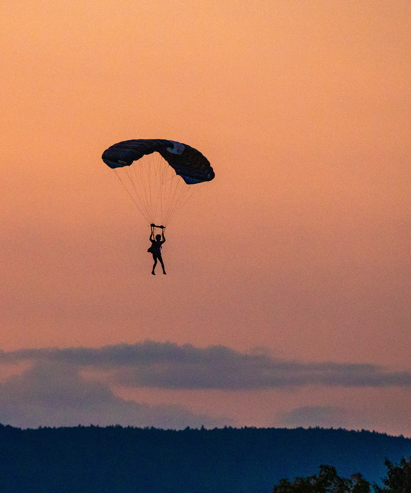 A canopy pilot silhouetted against an orange sky over forested hills